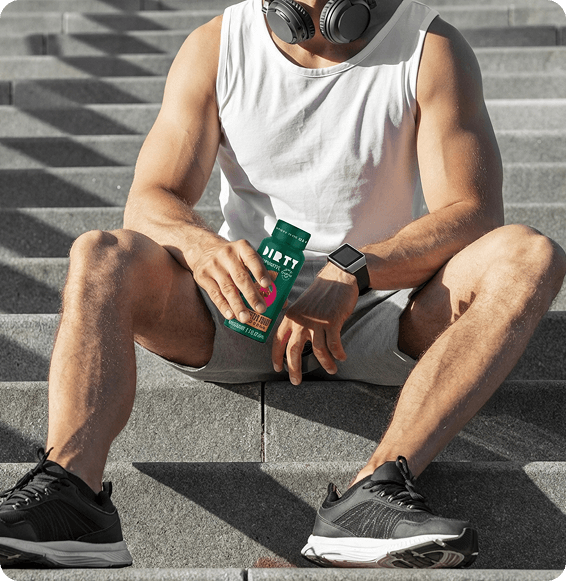 Person sitting on outdoor steps holding a green dietary supplement bottle after a workout, wearing athletic apparel and headphones.