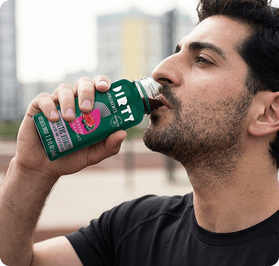 Man drinking from a green dietary supplement bottle outdoors, shown in close-up with an urban background.