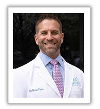 Dr Brian Paris smiling in a white lab coat with his embroidered name