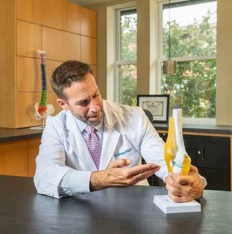 Dr Brian Paris in a lab coat examining an anatomical knee joint model