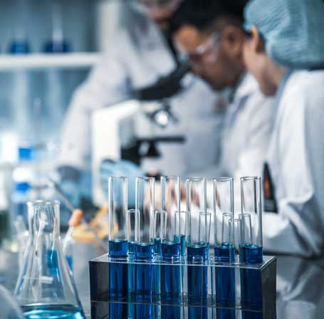 Researchers in lab coats and goggles behind a rack of blue test tubes