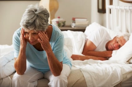 Woman holding her head sitting on a bed